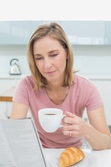 Woman reading newspaper while having coffee in kitchen