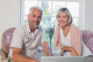 Smiling mature couple using laptop at home