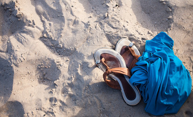 Slippers and blue textile on a sand