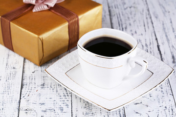 Cup of coffee and gift on wooden table close-up