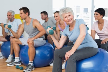 Fitness class with dumbbells sitting on exercise balls in gym