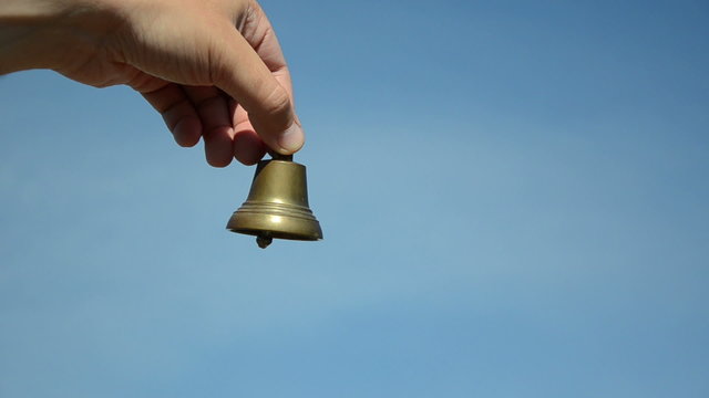 Male and female hands ding with silver bronze bell on blue sky