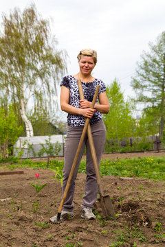 Cheerful smiling blonde with a shovel and rake in the garden