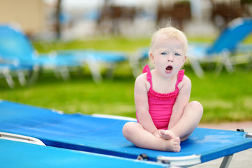 Fototapeta na wymiar Toddler girl sitting on a sunbed by a pool