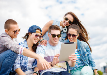 group of smiling teenagers looking at tablet pc