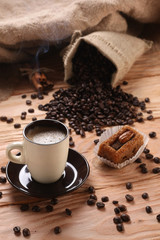 A hot cup of espresso with coffee beans and cinnamon on a wooden