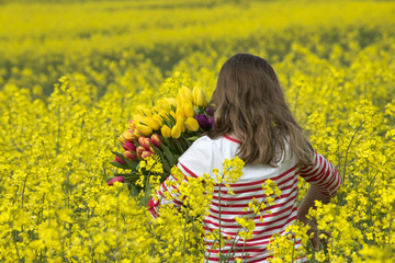 Child walking in a field of rapeseed holding Spring flowers