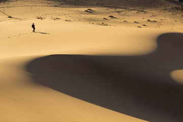 Fototapeta na wymiar Man walking on dunes in desert