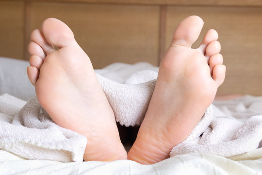 female feet sticking out of blanket on bed