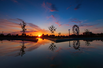 Naklejka premium Reflection of sunrise, silhoutte of trees and wheel over a lake