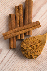 Cinnamon, whole sticks behind wooden spoon with a heap of powder