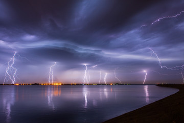 Naklejka na ściany i meble Thunderstorm and lightnings in night over a lake with reflaction