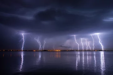 Selbstklebende Fototapete Sturm Gewitter und Blitze in der Nacht über einem See mit Reflexion