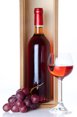 Obraz premium Bottles of wine in a wooden box with a glass of wine and red gra