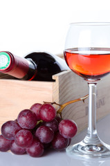 Bottles of wine in a wooden box with a glass of wine and red gra