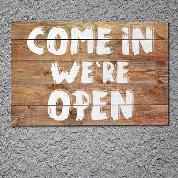 Vintage "Come in we`re open" wooden sign on stucco concrete wall