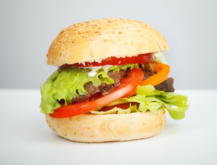 Big hamburger lays on the table above gray background