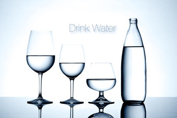 Glassware and bottle filled with water on white background