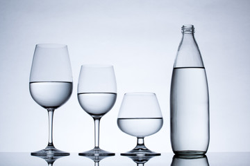 Glassware and bottle filled with water on white background