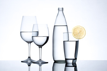 Glassware and bottle filled with water on white background