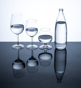 Glassware and bottle filled with water on white background