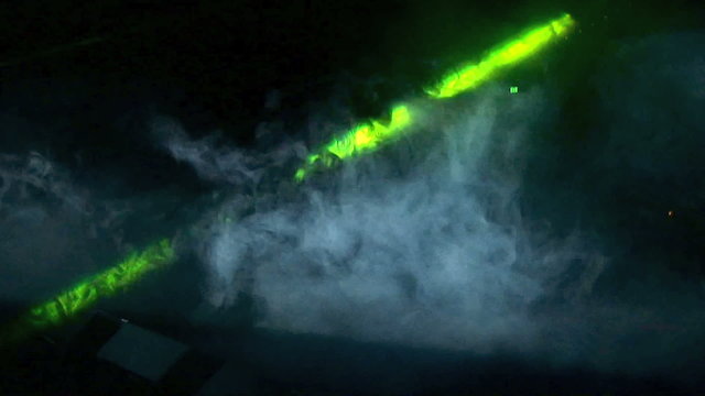 Green laser light flashing through clouds of smoke