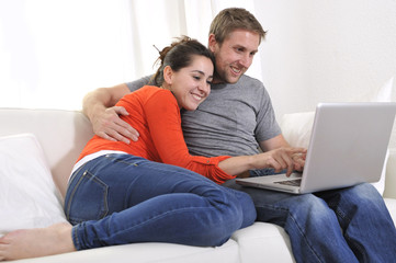 young happy couple at home working on computer on sofa