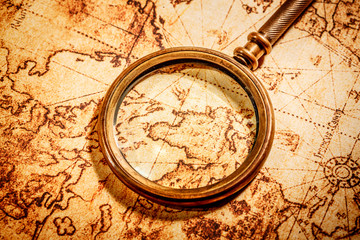 Vintage magnifying glass lies on an ancient world map