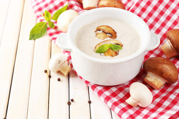 Mushroom soup in white pot, on napkin, on wooden background