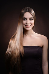 Fototapeta premium Beautiful young woman with long hair on dark brown background