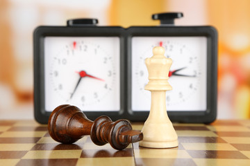 Chessboard with chess and clock on light background