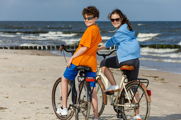 Obraz premium Teenage girl and boy biking on beach