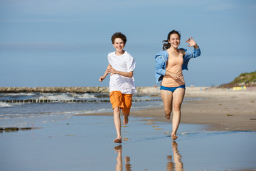 Teenage girl and boy running, jumping on beach