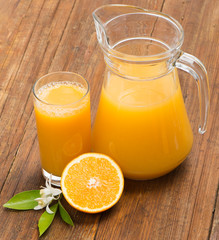 Obraz na płótnie Canvas Jug, glass of orange juice and orange fruits with green leaves a