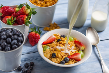 Pouring milk into cornflakes with fruits