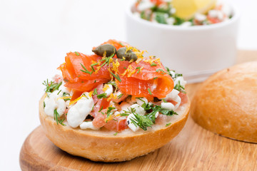 bun with cottage cheese, tomato and salmon on a wooden board