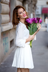 Fototapeta premium Cute girl in white dress and a beautiful bouquet of tulips.