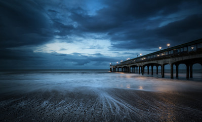 Twilight dusk landscape of pier stretching out into sea with moo