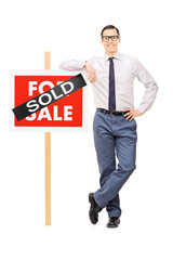 Male real estate agent leaning on a sold sign