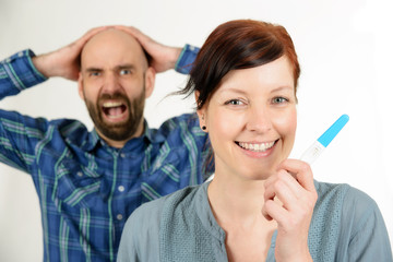 Lachende Frau und verzweifelter Mann mit Schwangerschaftstest