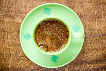 Green cup of black coffee on wooden table