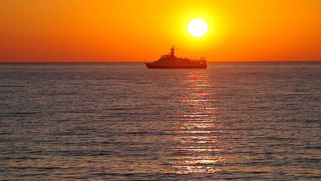 Cargo ship sailing away against colorful sunset