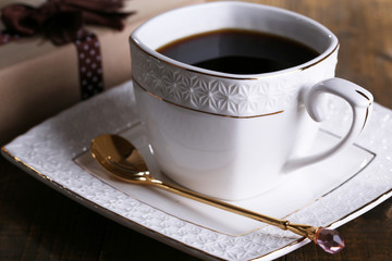 Cup of coffee and gift on wooden table close-up