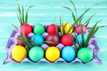 Colorful Easter eggs with grass in tray on wooden background