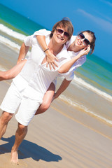 couple in sunglasses on holiday piggybacking cheerful on beach