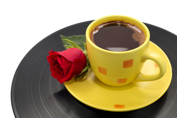 Yellow cup of coffee with beautiful red rose on black record