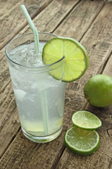 Cold drink with lime and ice on wooden table