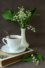 Bouquet of lilies of the valley, a book, a cup of coffee.