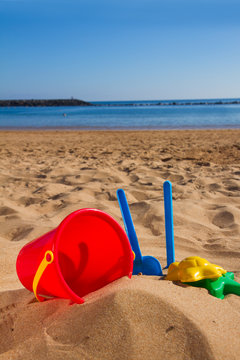 bucket with plastic beach toys in sand on sea shore