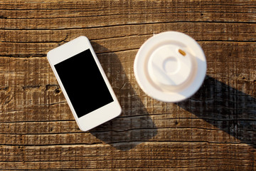White smart phone and coffee cup on wooden surface